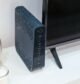 Home WiFi router placed next to a TV on a living room shelf